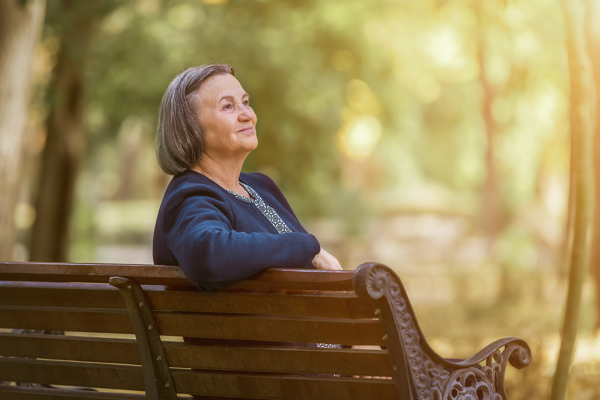 Frau auf einer Parkbank blickt verträumt mit einem Lächeln in die Ferne