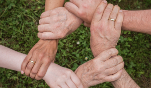 6 Hände unterschiedlicher Menschen greifen ineinander und formen eine Art Kreis