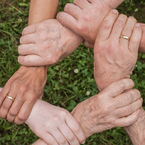 6 Hände unterschiedlicher Menschen greifen ineinander und formen eine Art Kreis