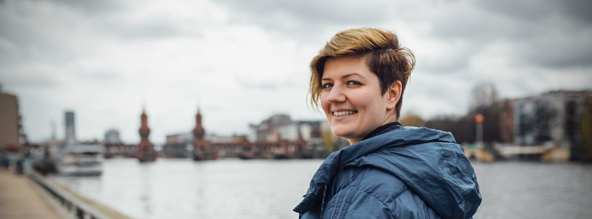 Franziska Krause in Berlin vor der Oberbaumbrücke und der Spree, blickt lachend in die Kamera