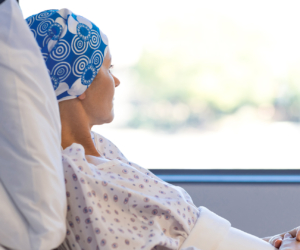 Frau mit Kopftuch nach Chemo schaut vom Krankenhausbett aus dem Fenster