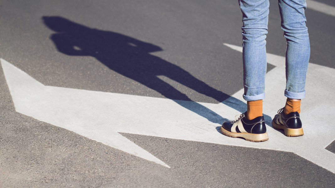 Nahaufnahme einer jungen Frau in schwarzen Schuhen und blauen Jeans, die auf einer Straße mit Abbiegespurpfeilen steht, die in verschiedene Richtungen zeigen - Konzept für Lebensentscheidungen