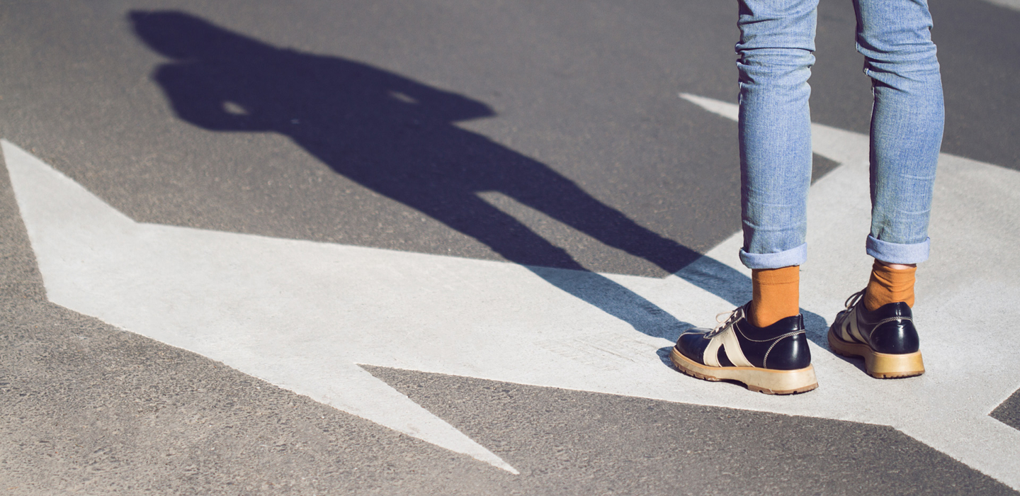 Nahaufnahme einer jungen Frau in schwarzen Schuhen und blauen Jeans, die auf einer Straße mit Abbiegespurpfeilen steht, die in verschiedene Richtungen zeigen - Konzept für Lebensentscheidungen