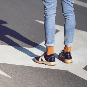 Nahaufnahme einer jungen Frau in schwarzen Schuhen und blauen Jeans, die auf einer Straße mit Abbiegespurpfeilen steht, die in verschiedene Richtungen zeigen - Konzept für Lebensentscheidungen