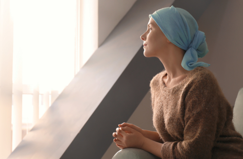Frau nach Chemotherapie mit Kopftuch blickt aus Fenster