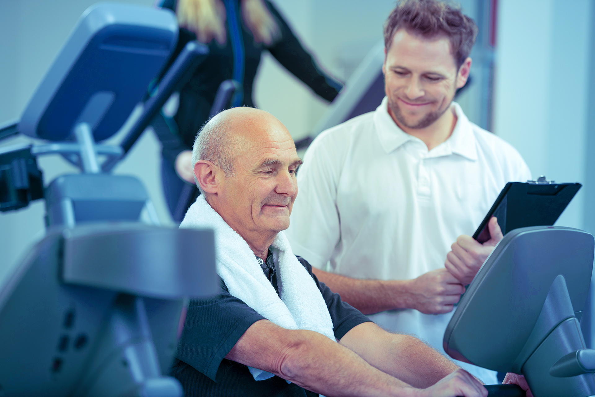 Reha-Trainer betreut älteren Patienten auf einem Fitnesgerät