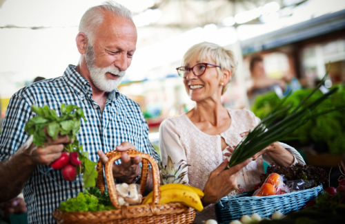 älteres Ehepaar beim Einkaufen mit Körben voller frischem Gemüse