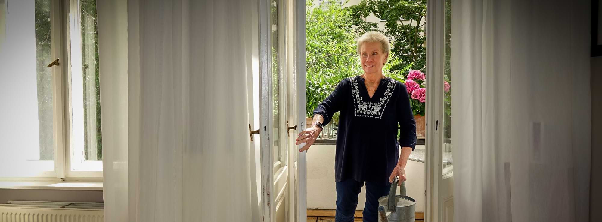 Susanne Kranz kommt mit einer Gießkanne vom Balkon in die Wohnung zurück