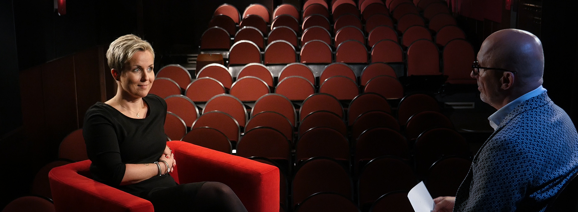 Nadja Will sitzt auf einer Theaterbühne im Roten Sessel für ein Interview