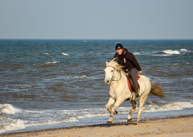 Frau reitet mit Pferd am Strand