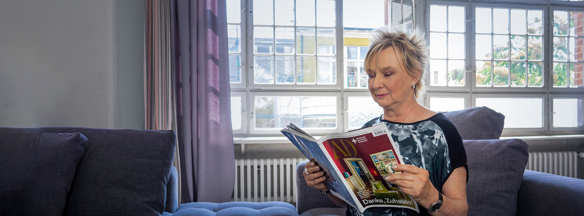 Sabine Schneider sitzt auf der Couch in einem Loft und liest ein Magazin