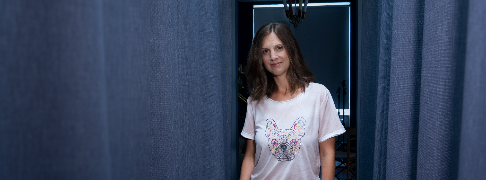 Janina Seifert steht im Ankleidezimmer mit einem weißen T-Shirt mit Hunde-Applikation und lächelt in die Kamera